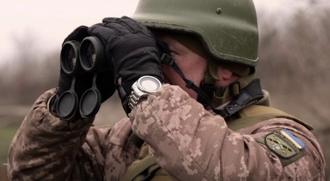 Український військовий у камуфляжі дивиться у бінокль на тлі зимового пейзажу