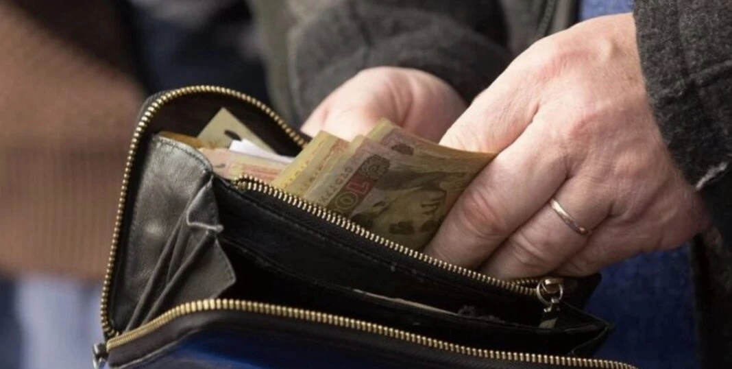 Руки людини, яка тримає відкритий шкіряний гаманець з купюрами по 100 гривень