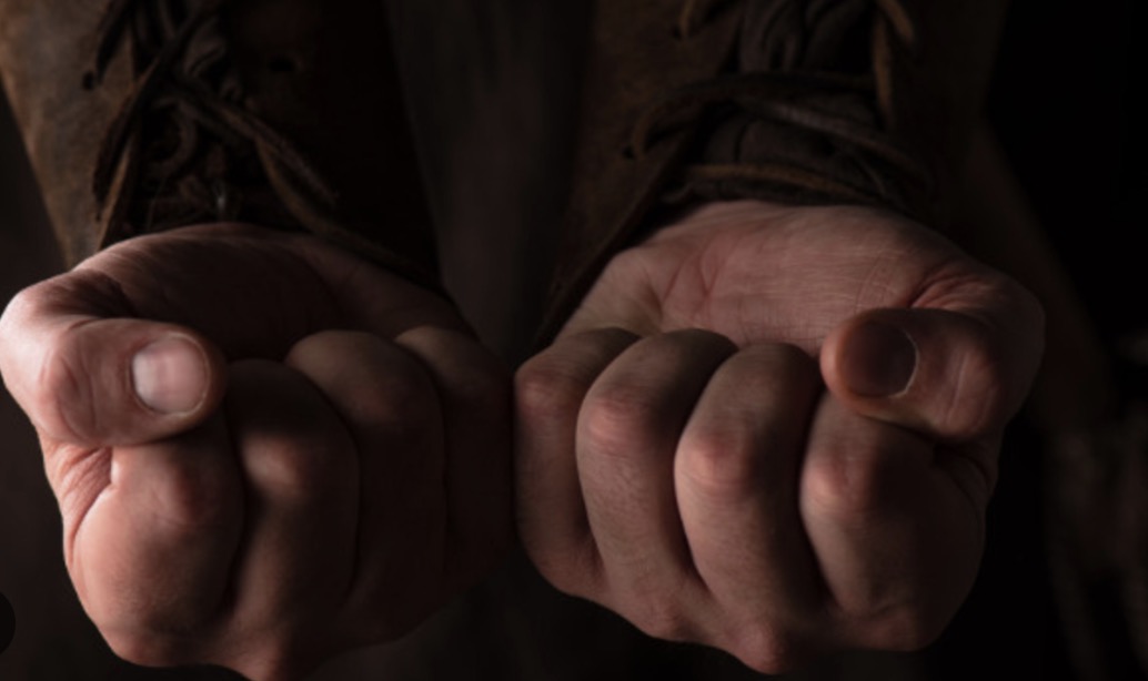 Побиття дитини на Житомирщині: агресивний напад сусіда Стиснуті чоловічі кулаки на темному фоні, що символізують агресію та насильство