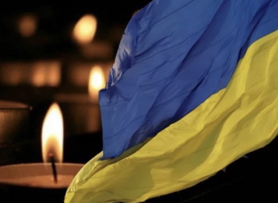 Синьо-жовтий прапор України поруч із запаленою свічкою пам'яті у темряві