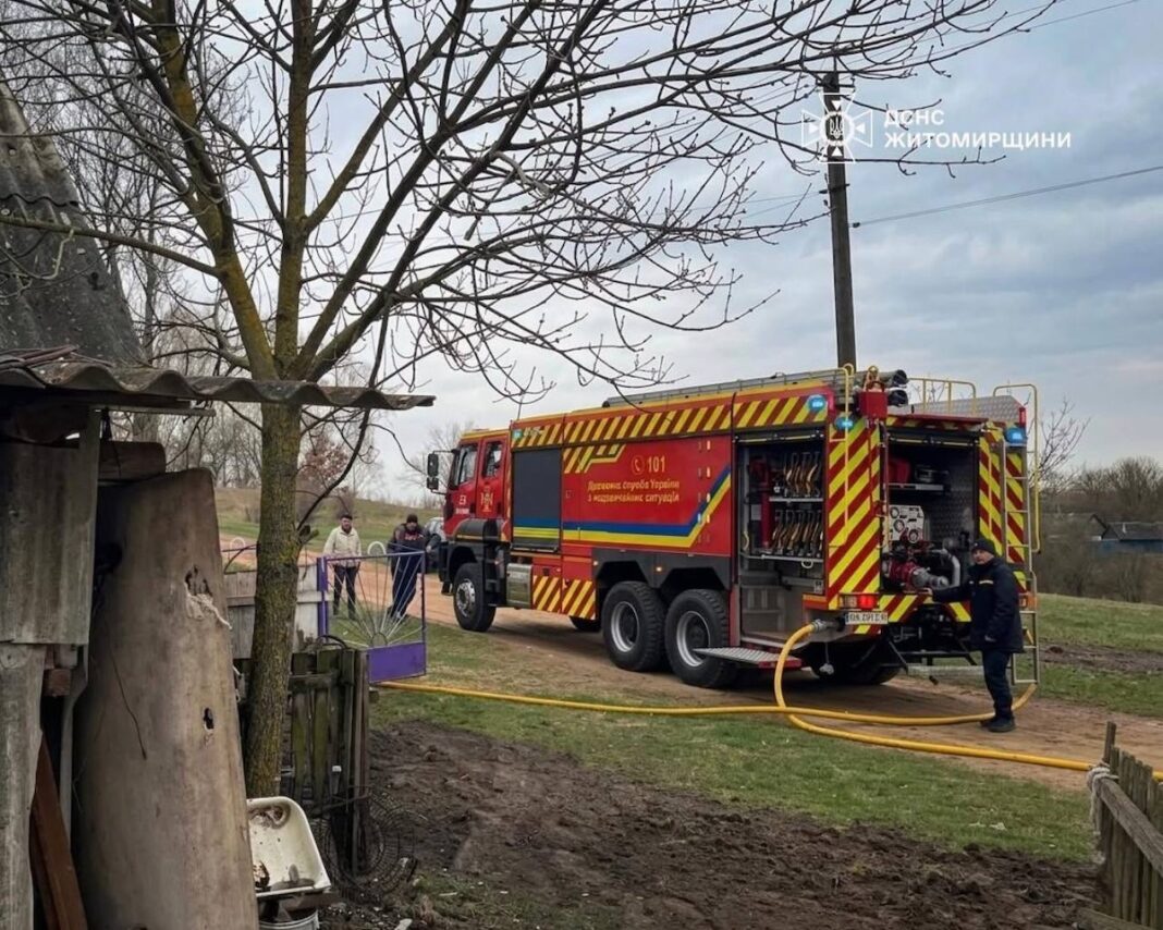 Робота рятувальників ДСНС у Житомирській області Червоний пожежний автомобіль ДСНС України з розгорнутим жовтим рукавом стоїть на сільській ґрунтовій дорозі біля паркану