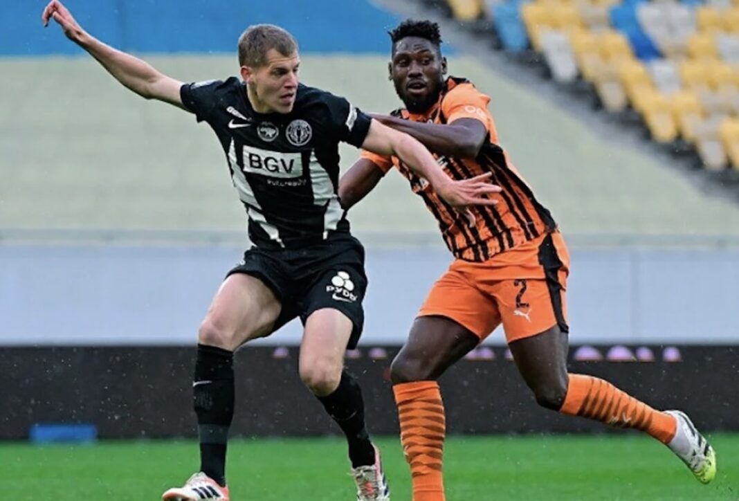 Гравець житомирського «Полісся» у чорній формі та футболіст донецького «Шахтаря» в оранжево-чорній формі ведуть боротьбу за м'яч