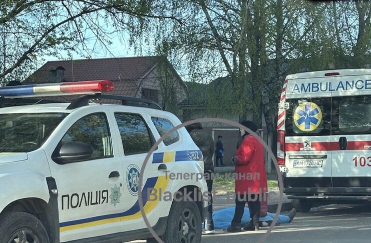 Поліцейський автомобіль Renault та карета швидкої допомоги Peugeot припарковані біля накритого блакитною тканиною тіла людини на вулиці