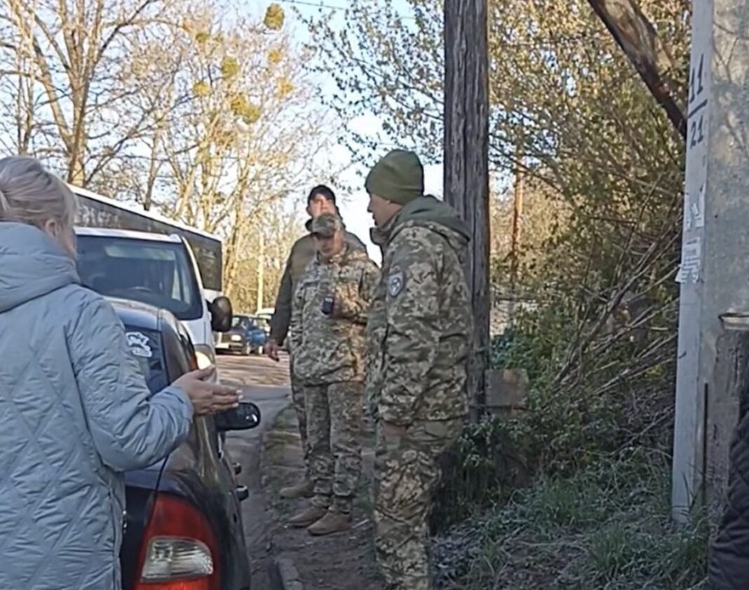 Жінка емоційно спілкується з трьома чоловіками у військовій формі на узбіччі дороги біля автомобіля