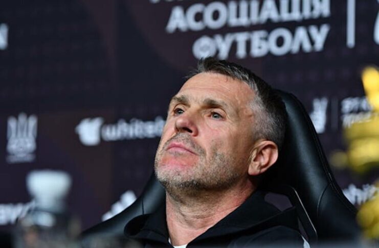 Сергій Ребров із зосередженим виразом обличчя сидить у чорному кріслі під час пресконференції на тлі офіційного банера УАФ