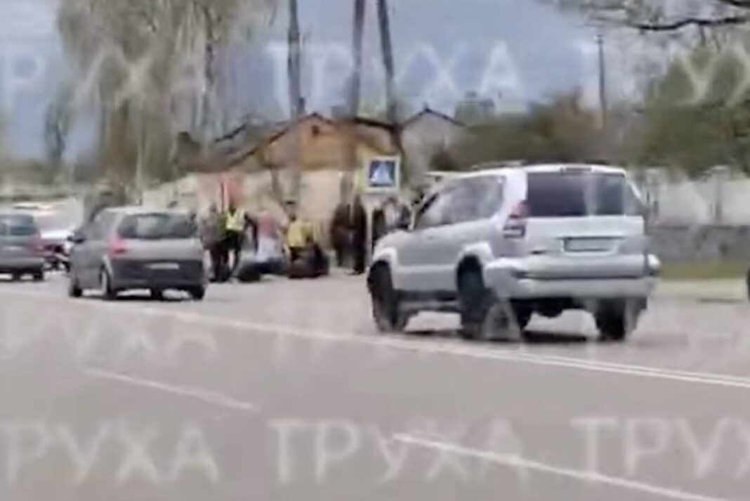 На проїжджій частині біля знаку пішохідного переходу зібралася група людей у світловідбивних жилетах, які надають допомогу постраждалому, поруч проїжджають автомобілі