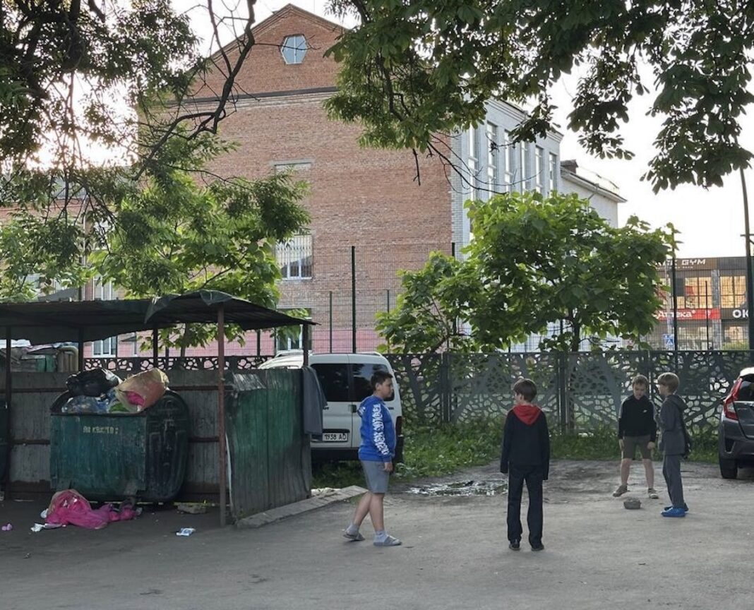 Група хлопчиків стоїть на асфальті поруч із контейнерами для сміття біля будівлі ліцею №3 у Житомирі